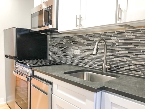 A kitchen with a black microwave above a stove and a silver sink.