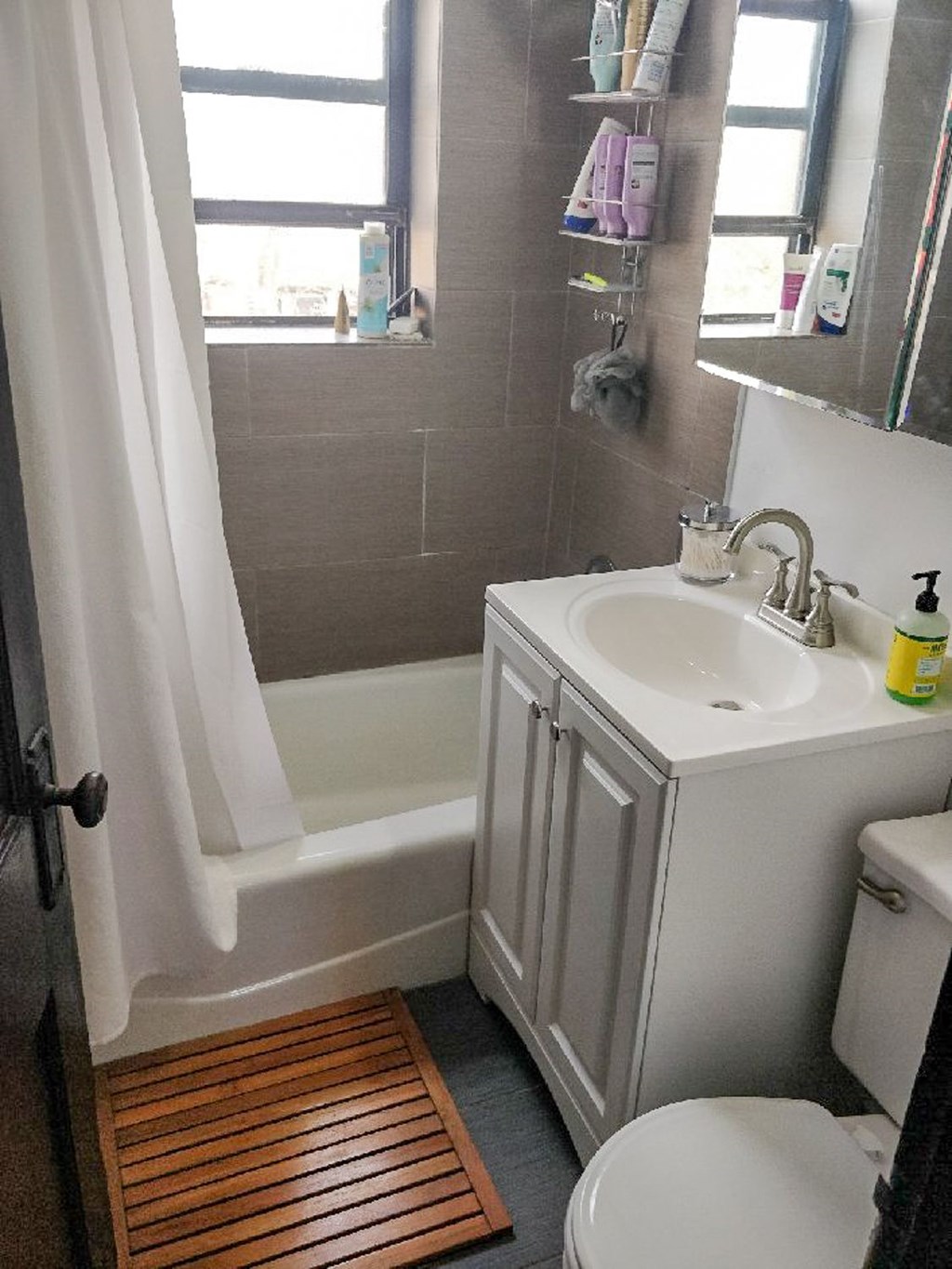 A white sink with a wooden mat on the floor.