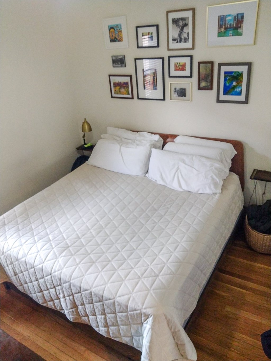 A bed with a white comforter and two pillows with a wall of framed pictures above it.