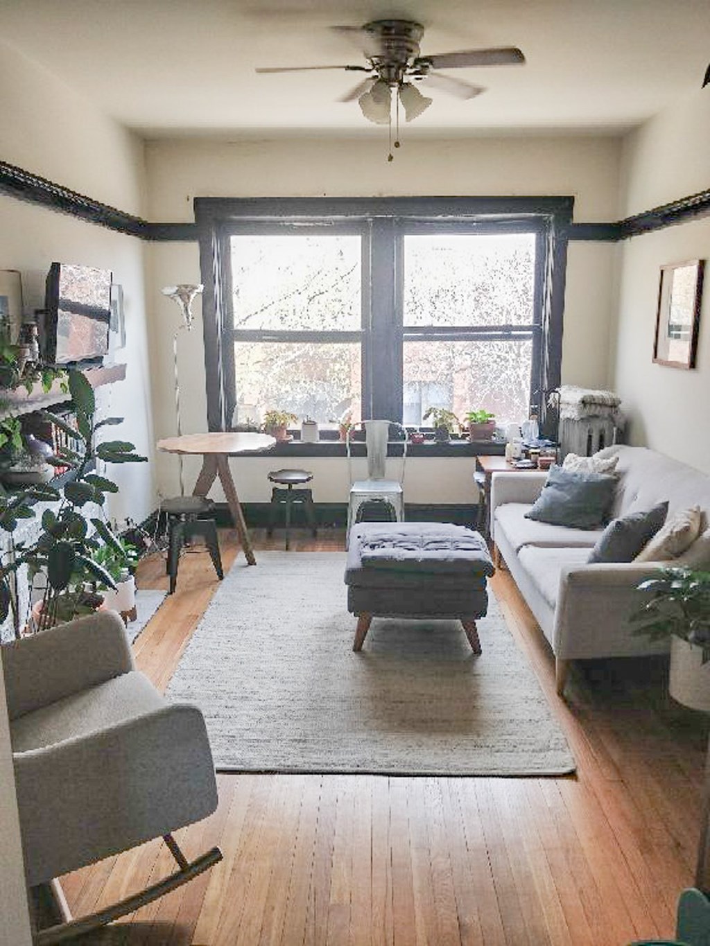 A living room with a grey couch, a grey chair, a grey ottoman, a wooden floor, a wooden table, a wooden coffee table, a white couch, a white chair, a white coffee table, a white table, a