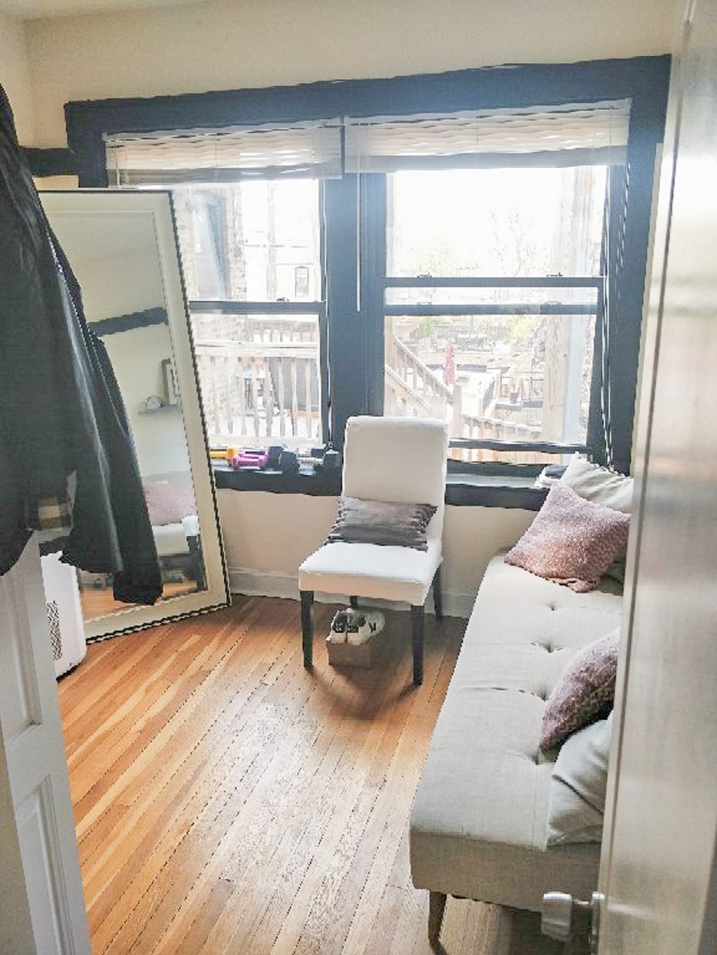 A white couch with pink pillows sits in a room with a large window.