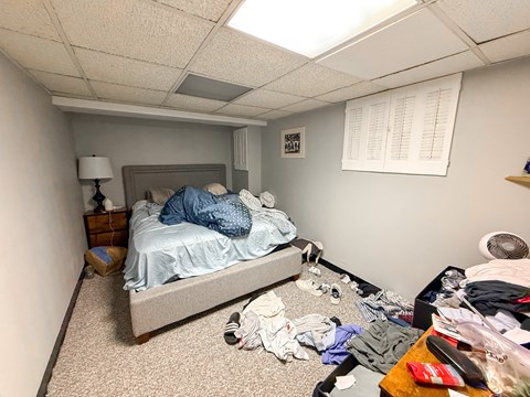 A messy bedroom with a bed, dresser, and clothes scattered on the floor.