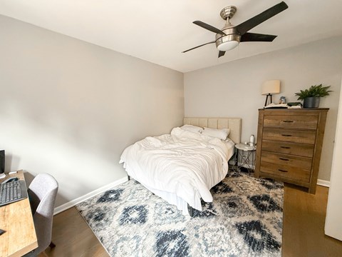 A bedroom with a bed, a dresser, a ceiling fan, and a rug.
