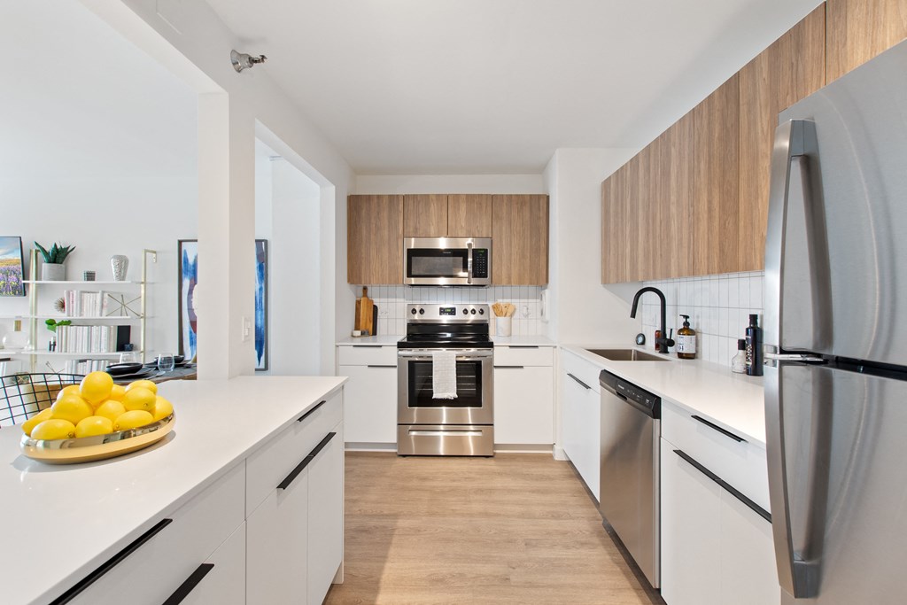 A kitchen with white countertops, modern blown cabinets, and brand new stainless steel appliances