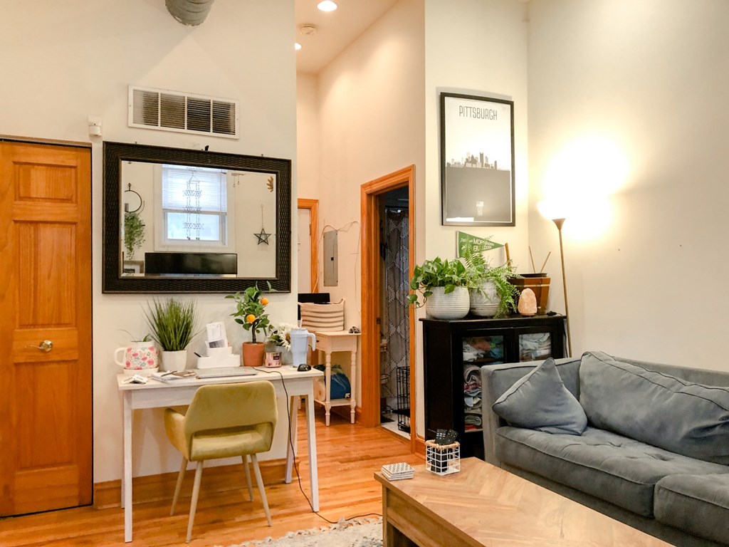 A living room with a grey couch, a white desk, and a wooden floor.