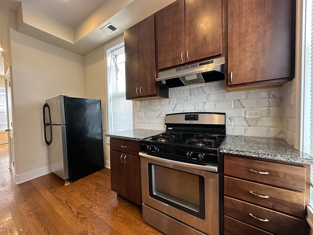 A kitchen with a black fridge, stove, and wooden cabinets.