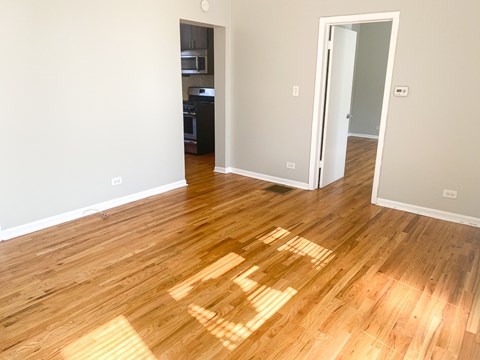 A room with wooden floors and a kitchen in the background.