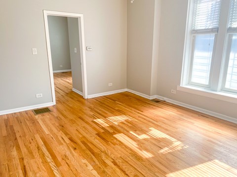 A room with wooden flooring and a window letting in sunlight.