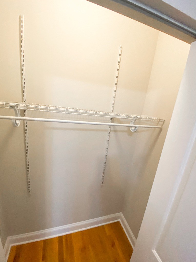 a walk in closet with white walls and a wood floor