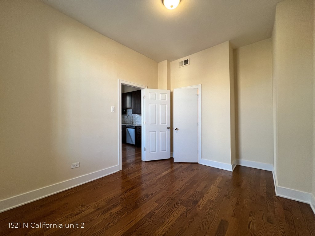 an empty living room with wood floors and a door to a bathroom