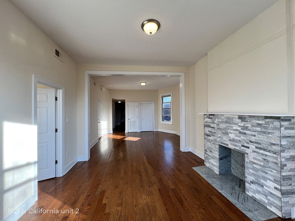 an empty living room with a stone fireplace and wooden floors