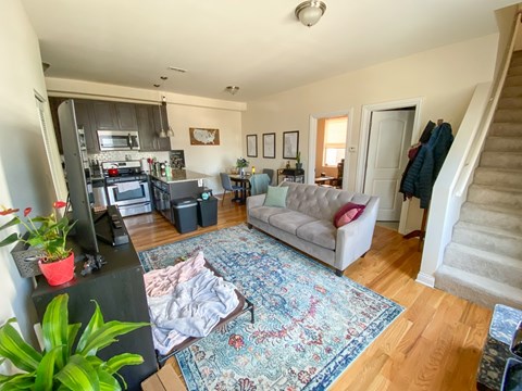 A living room with a rug on the floor and a staircase on the right.