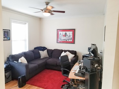 A living room with a grey couch, a red rug, and a ceiling fan.