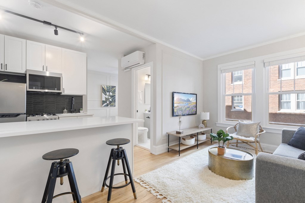 a living room with bar stools in front of a kitchen and a living area