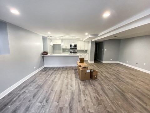 A room with wooden flooring and a kitchen area in the background.