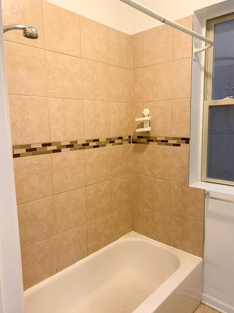A white bathtub in a bathroom with beige tiles.