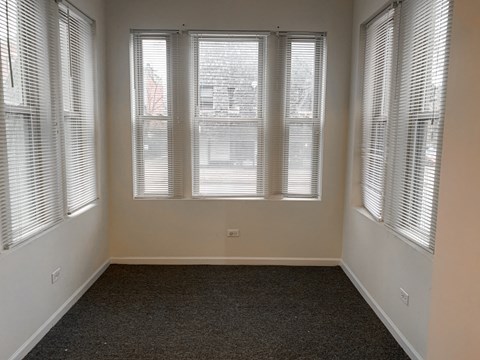 A room with a carpeted floor and three windows covered with blinds.