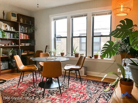 A living room with a round table surrounded by chairs and a bookshelf filled with books.