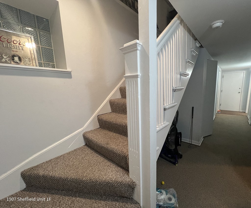 a stairwell with carpeted stairs and a white railing and a staircase leading up