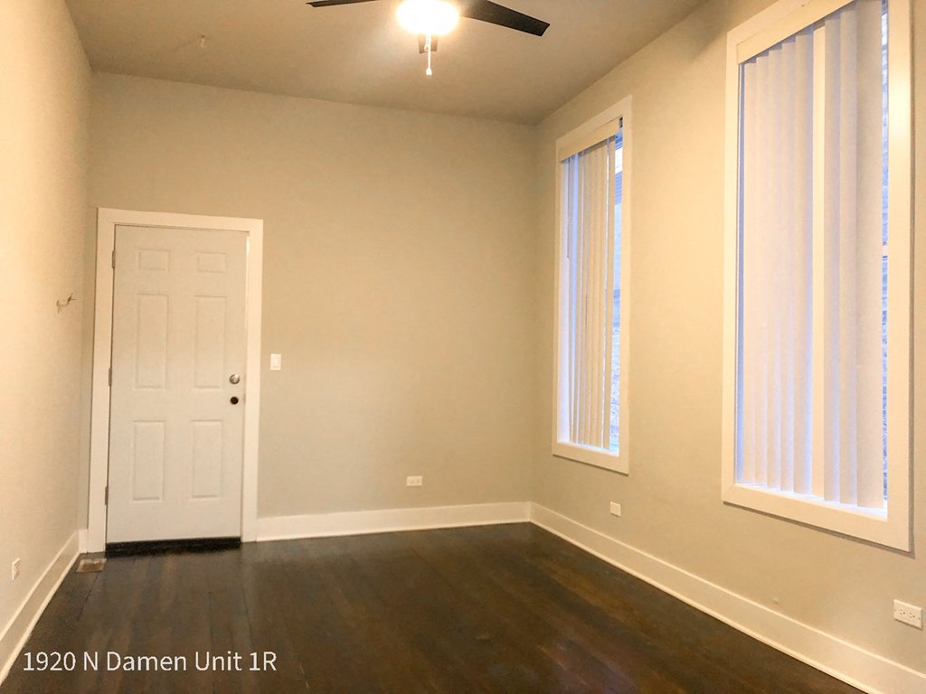 an empty living room with a white door and two windows