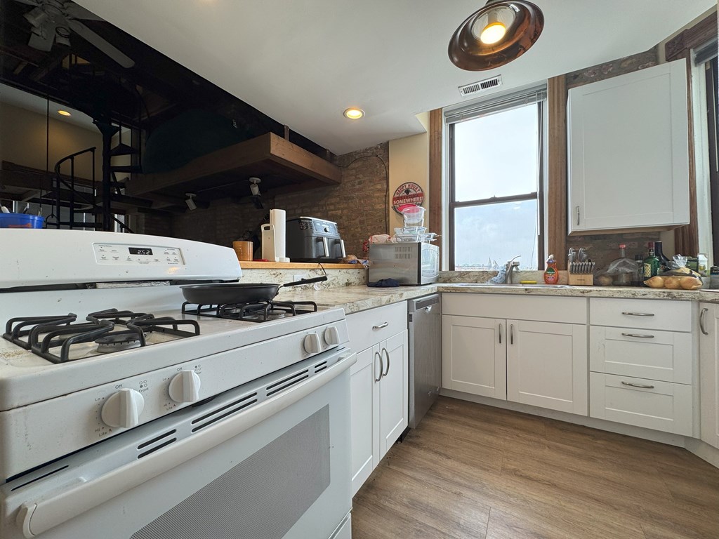 A white gas stove in a kitchen with wooden floors and white cabinets.
