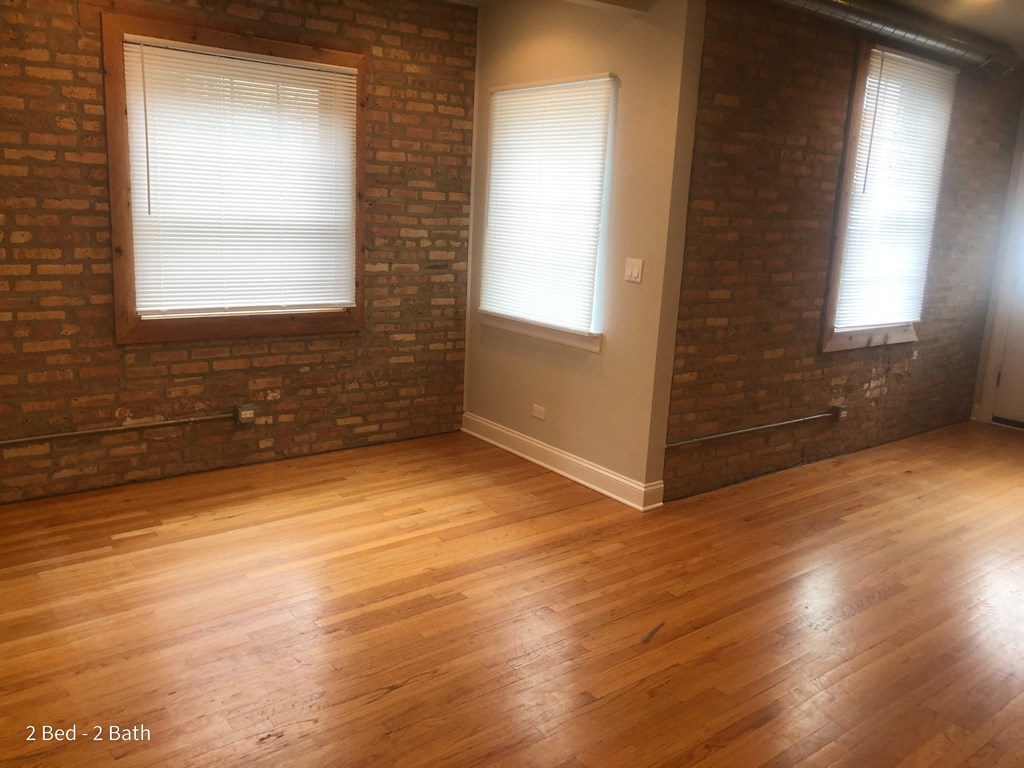 an empty living room with a wood floor and brick walls