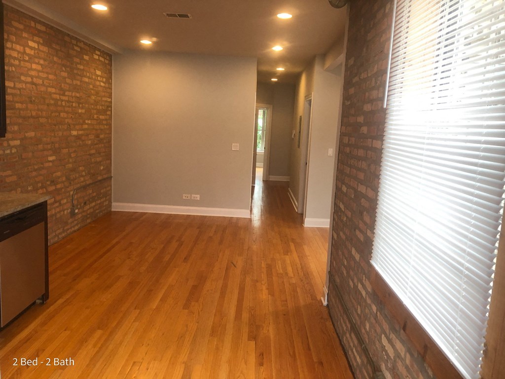 an empty living room with wood floors and a brick wall