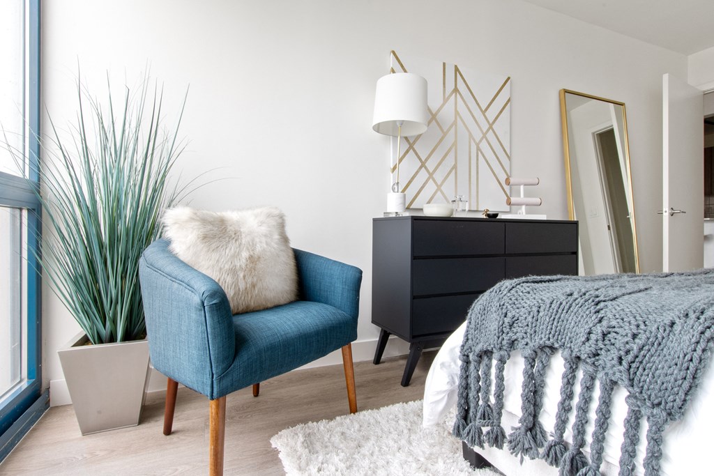 A bedroom with a blue modern chair and a black dresser