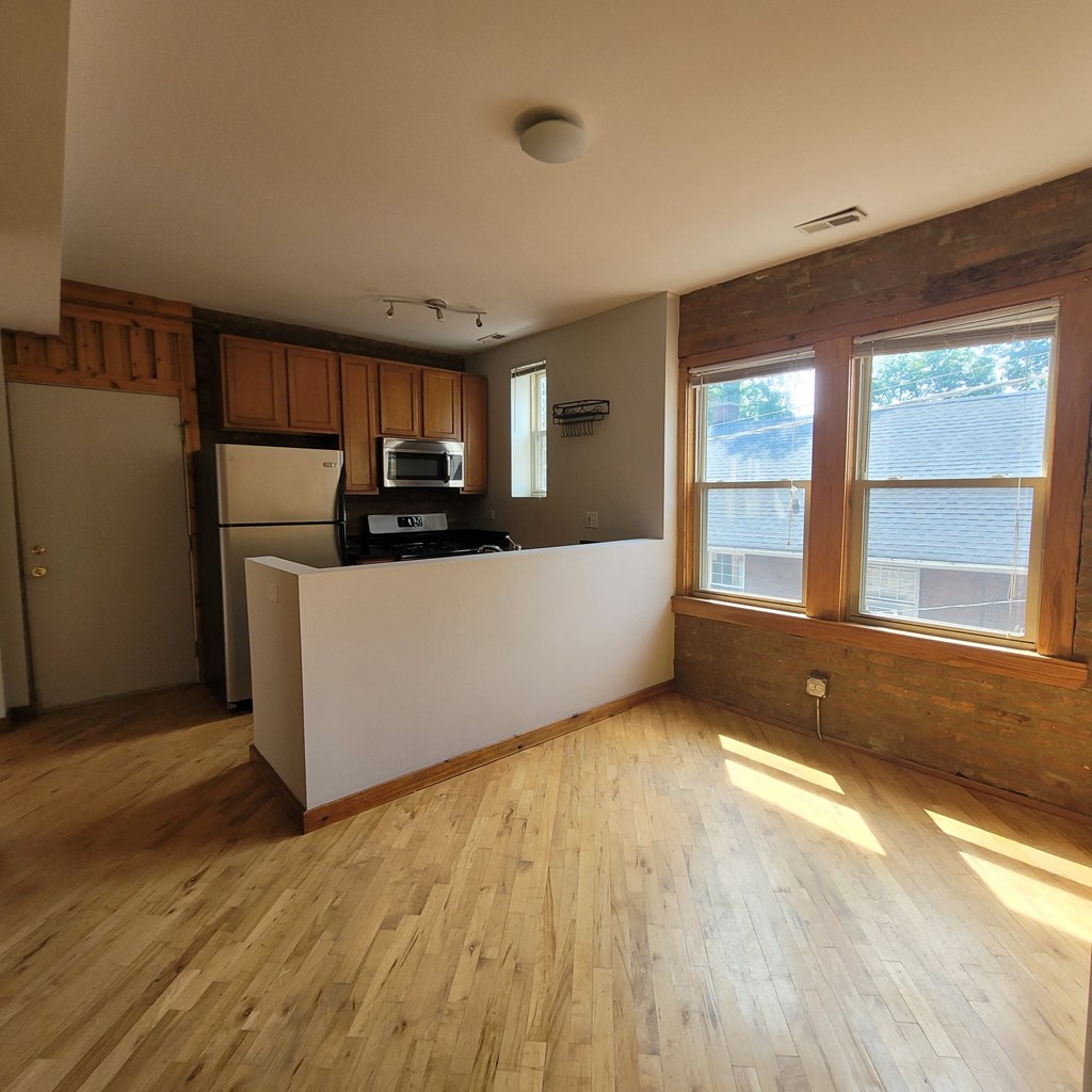 an empty living room with wood floors and a kitchen