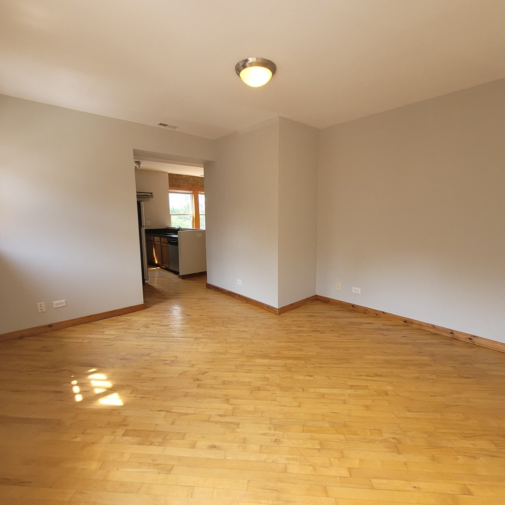 an empty living room with wooden floors and a kitchen