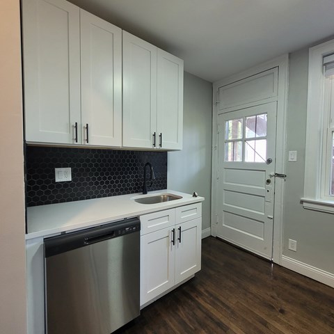 A kitchen with white cabinets and a black backsplash.