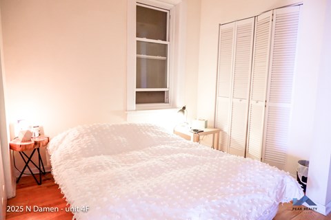 A bedroom with a large bed and a window with blinds.