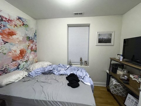 A bedroom with a bed, a TV, and a window with blinds.