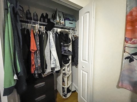 A white closet with clothes hanging on a rail.