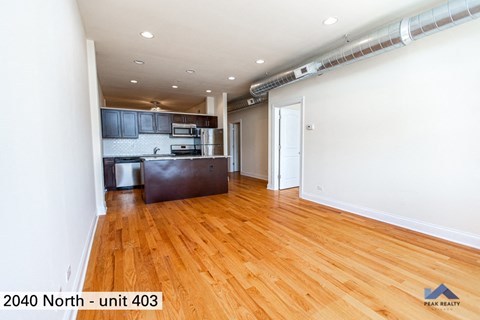 the living room of an apartment with wood floors and a kitchen