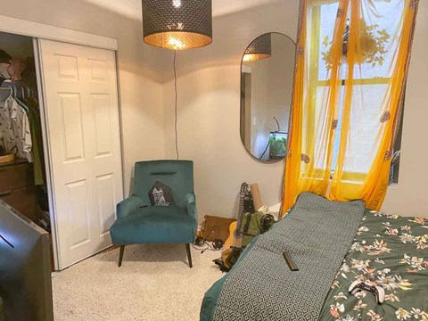 A bedroom with a bed, chair, and mirror.