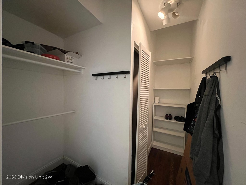 a walk in closet with white walls and shelves and a white closet door