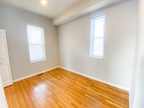 A room with wooden flooring and two windows.