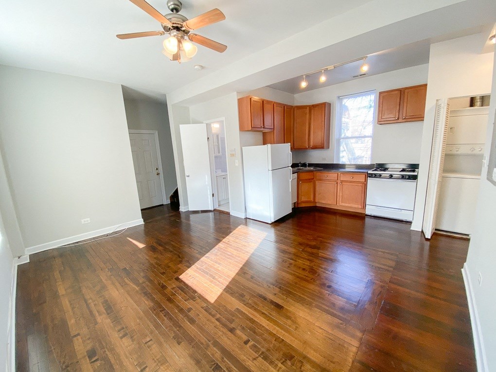 an empty living room and kitchen with wood flooring and a ceiling fan