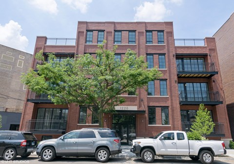 A red brick building with a tree in front and cars parked in front.