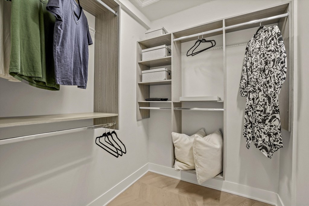 a walk in closet with white walls and shelves and a hanging rack with clothes