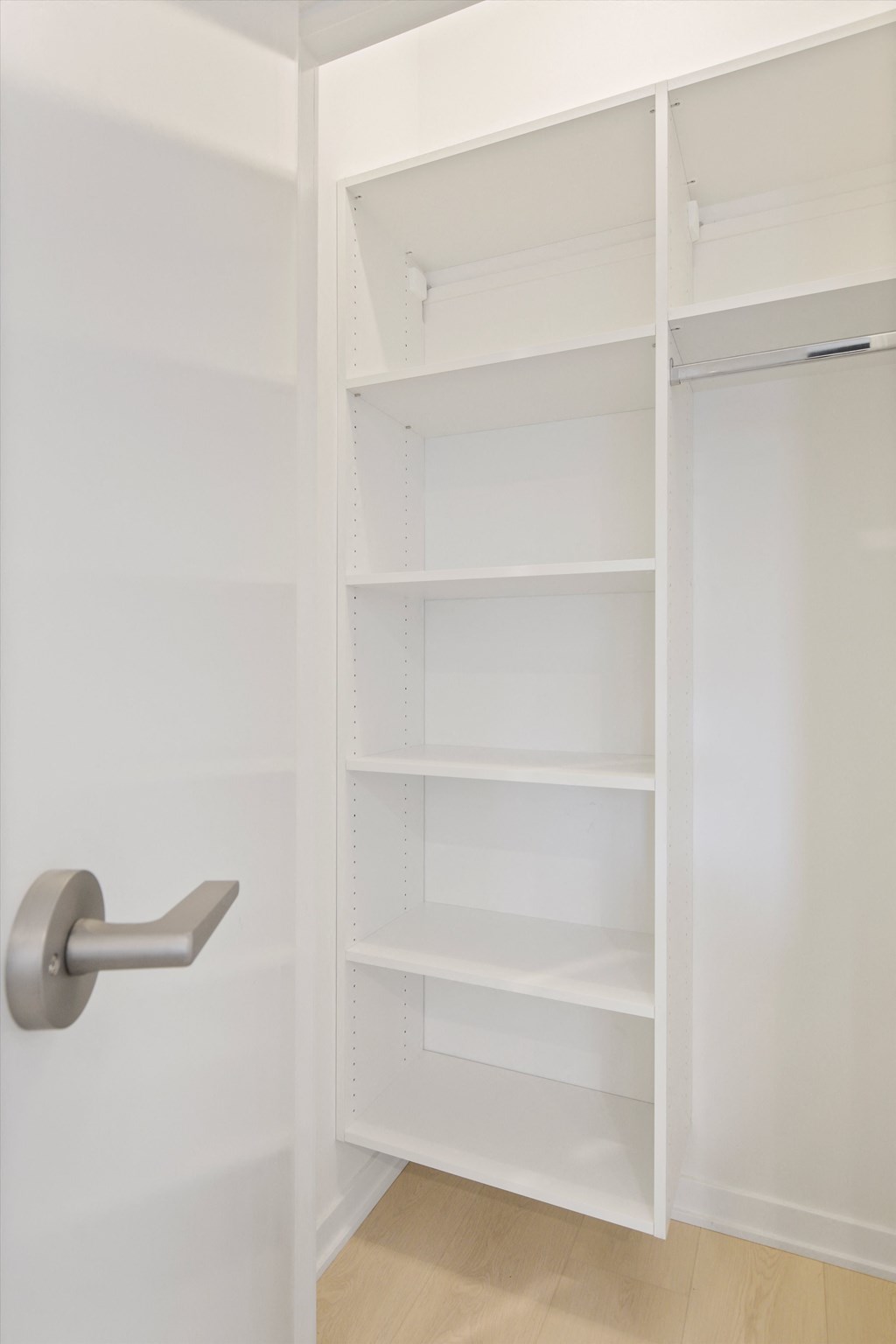 a closet with white shelves and a door with a silver handle