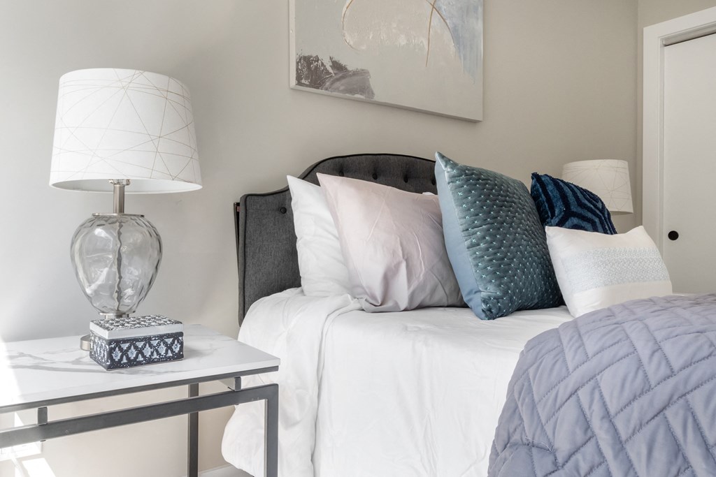 a white bed with blue and white pillows and a nightstand with a lamp