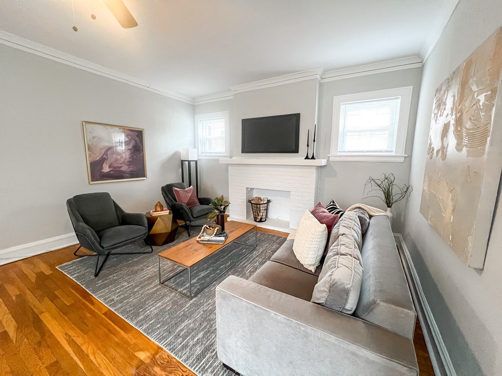 A living room with a grey couch, a black chair, a wooden floor, a fireplace, and a painting on the wall.