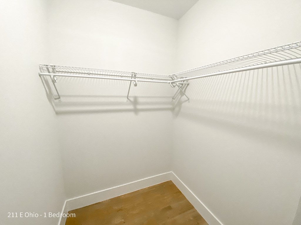 a walk in closet with white walls and a wood floor