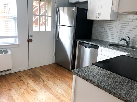 A kitchen with a stainless steel refrigerator and a black granite countertop.