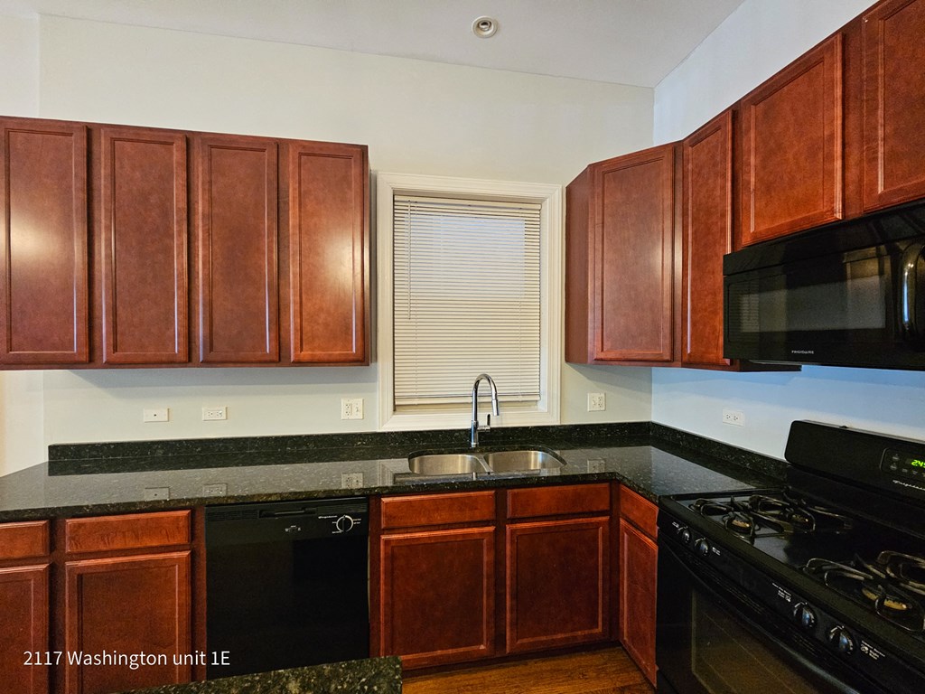 a kitchen with wooden cabinets and black counter tops and black appliances