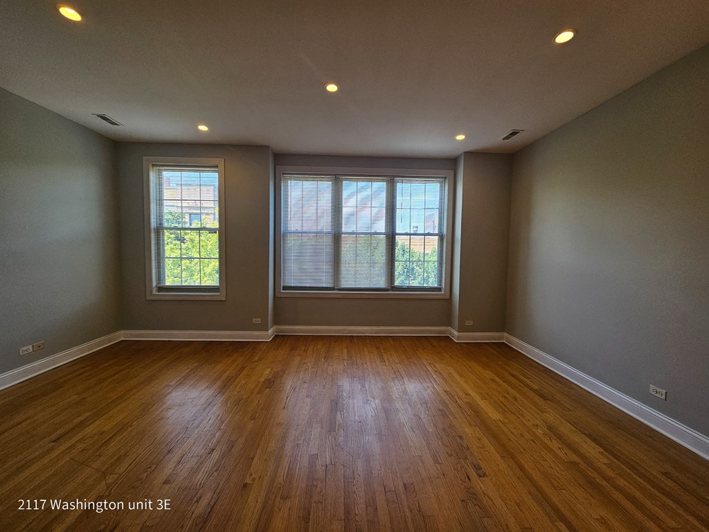 an empty living room with wood floors and two windows