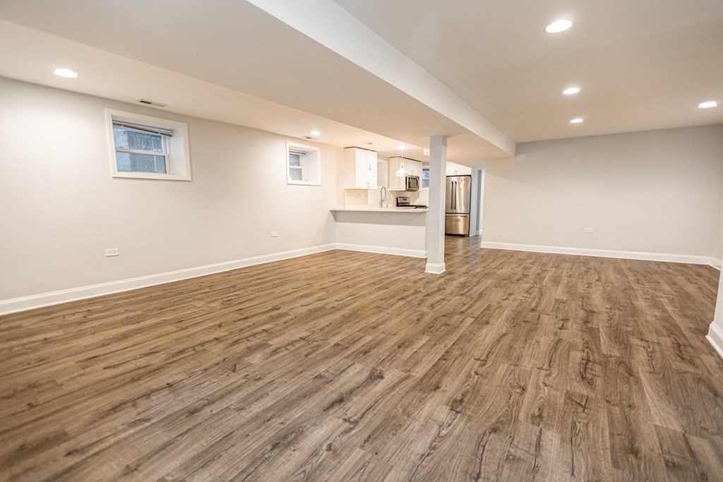 A room with wooden flooring and a kitchenette in the background.