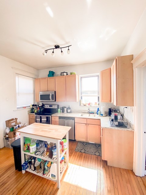 A kitchen with wooden floors and a table with a black trash can underneath it.